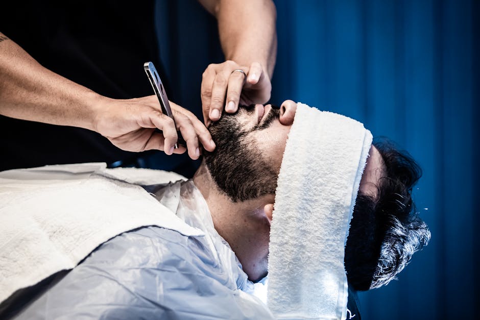 A barber applying a hot towel to a client's face during a traditional shave